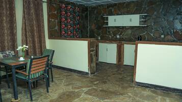 A stone-floored room with a dining table and chairs, a patterned curtain, and a stone wall with a decorative hanging.