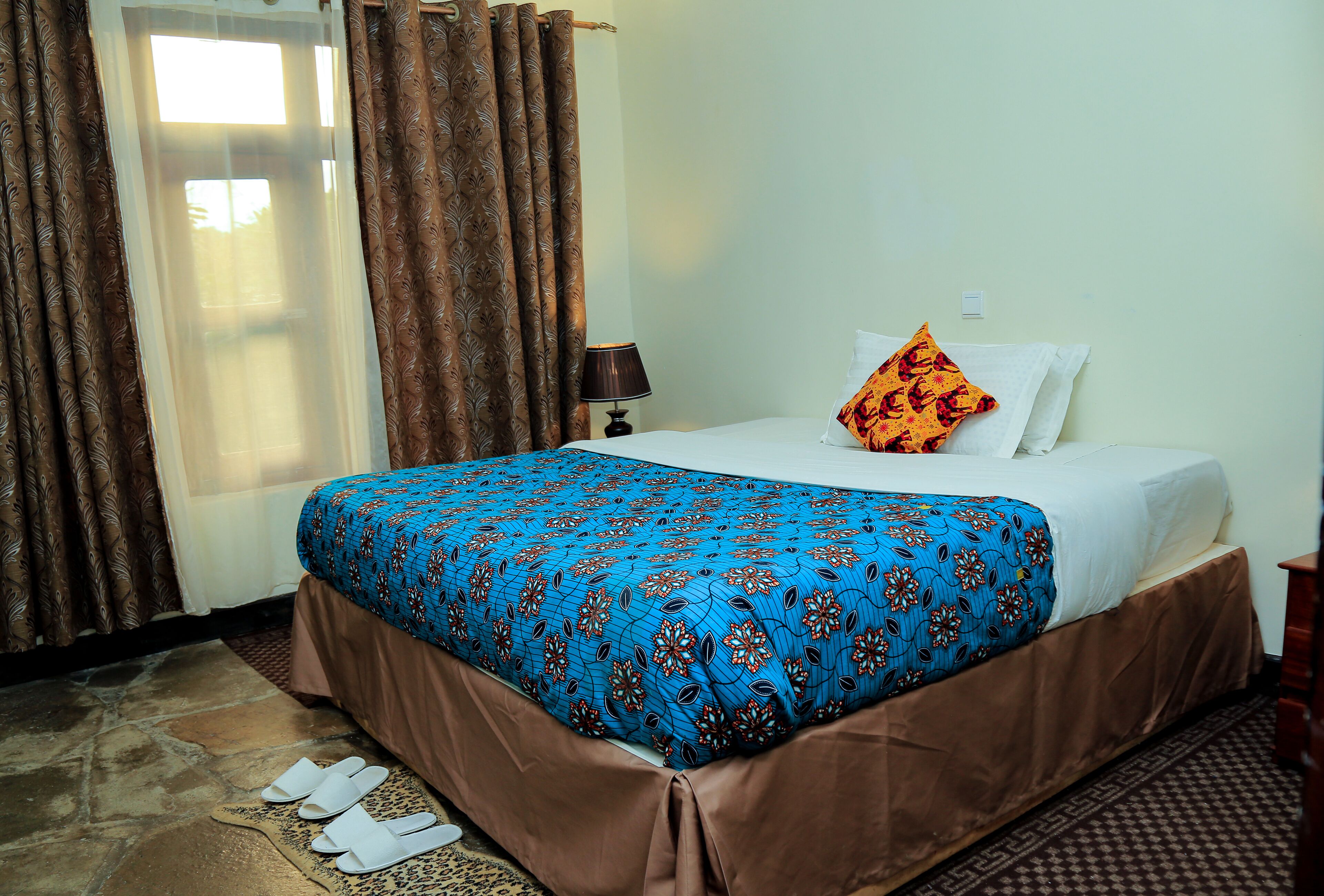 A hotel room with a bed, a nightstand, a lamp, and a window with curtains.