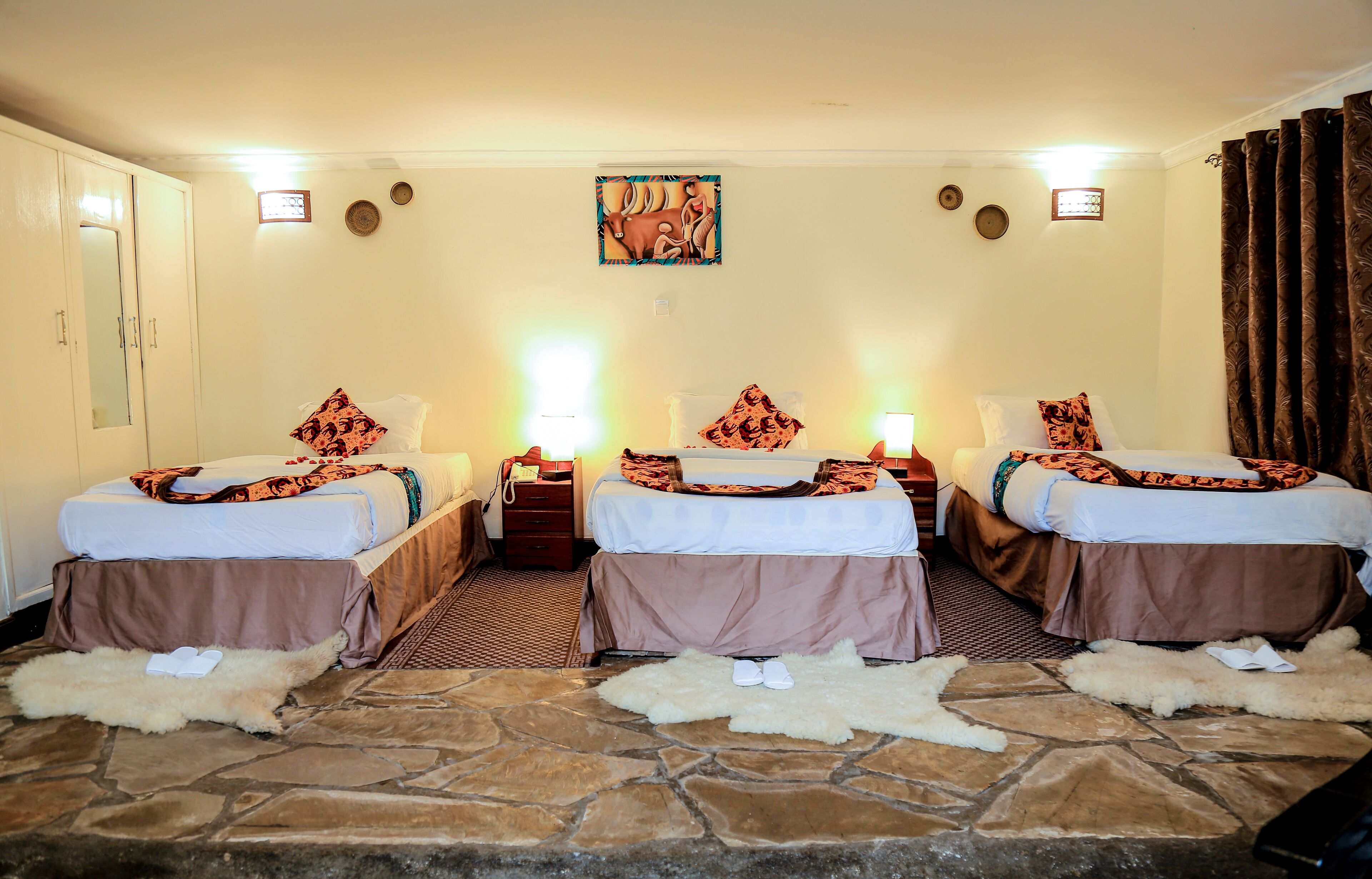 Habitación de hotel con tres camas, piso de piedra y un cuadro grande en la pared.
