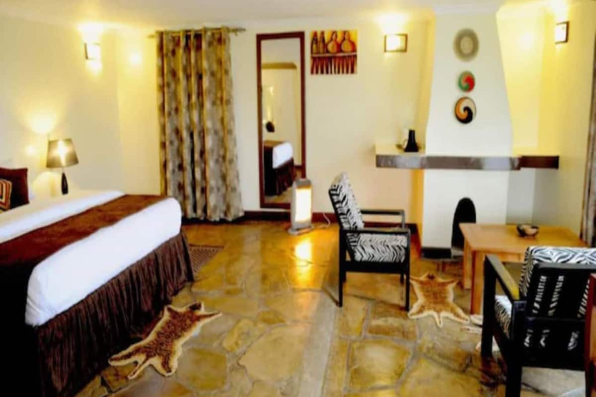 A hotel room with a bed, a desk, a chair, a mirror, and a fireplace.