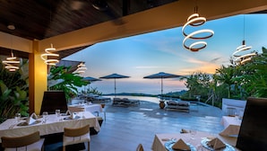 An outdoor dining area with tables set for two, surrounded by large umbrellas and plants, overlooking a scenic view. - Golden Pineapple Villas (Bahía Ballena)