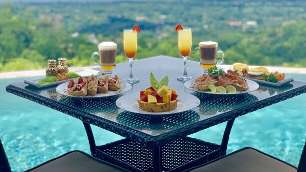 A table with food and drinks overlooking a pool and scenic view. - Golden Pineapple Villas (Bahía Ballena)