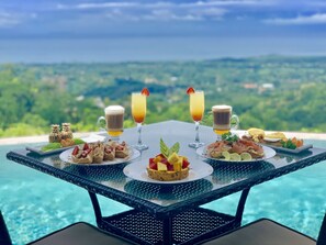 A table with food and drinks overlooking a pool and scenic view. - Golden Pineapple Villas (Bahía Ballena)
