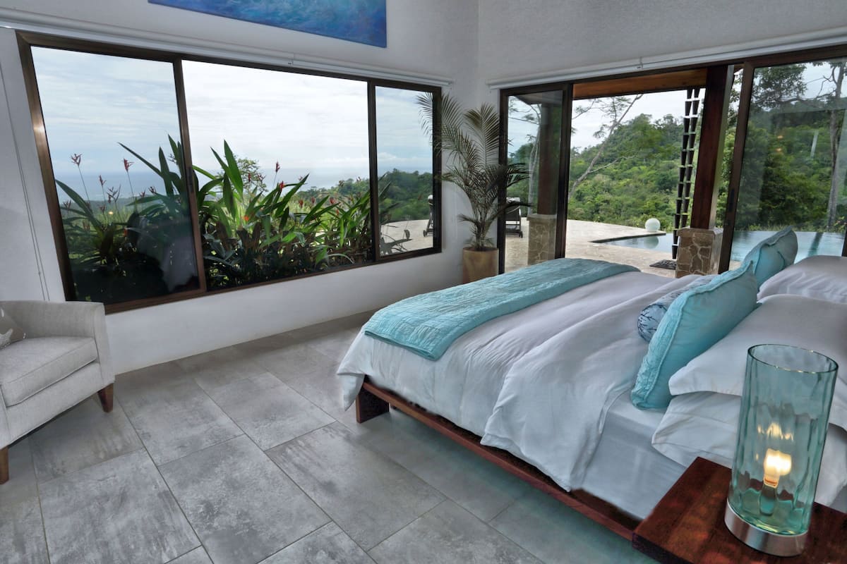 A bedroom with a large bed, a view of the outdoors, and a small table with a candle.
