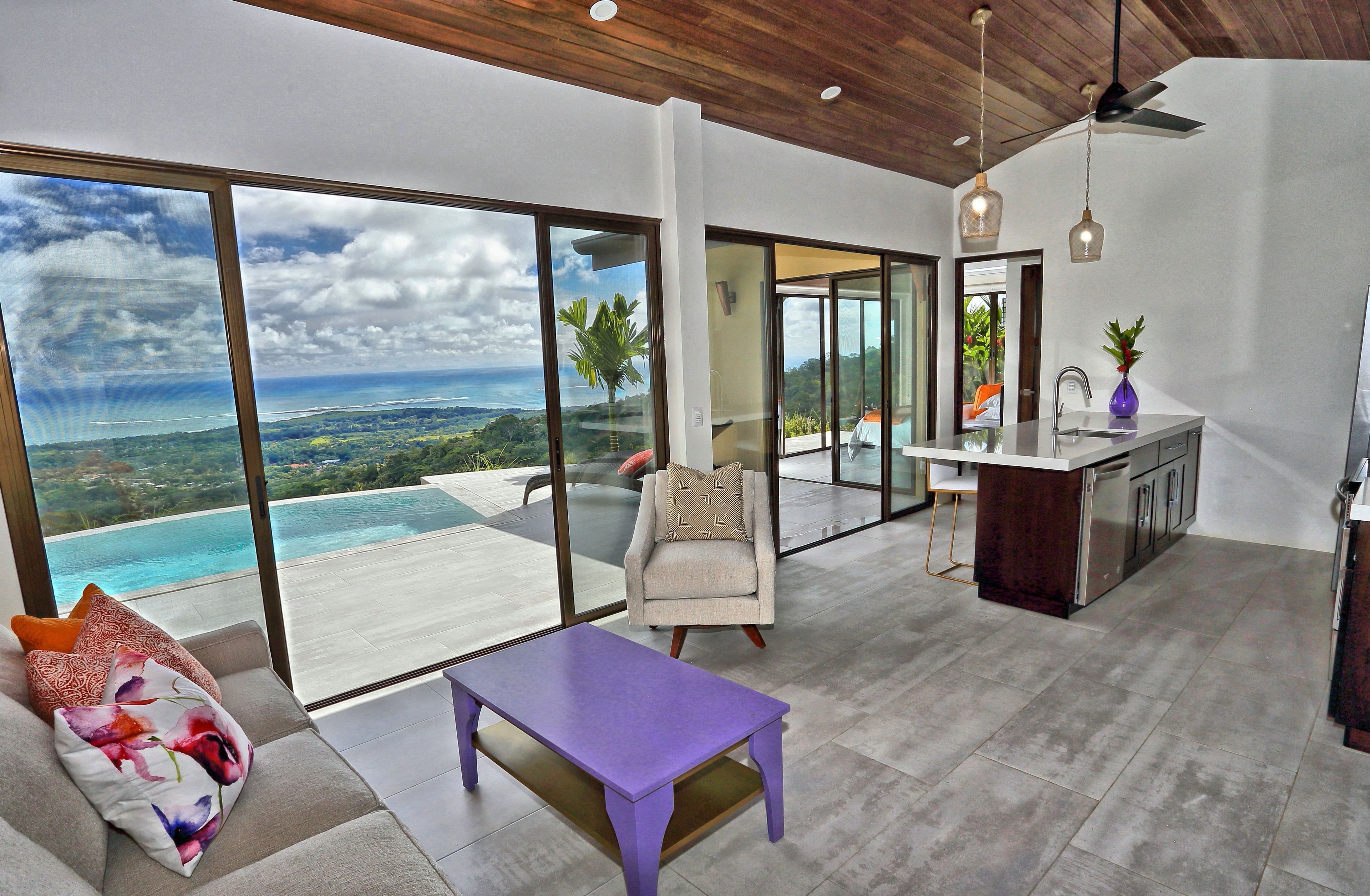 Un espace de vie moderne doté d’une grande porte vitrée donnant sur un balcon avec vue sur un paysage côtier.