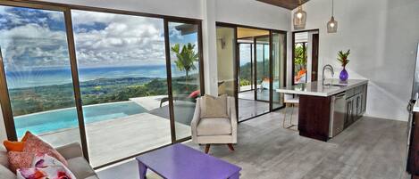 Un espace de vie moderne doté d’une grande porte vitrée donnant sur un balcon avec vue sur un paysage côtier.