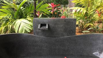 Una maceta de piedra negra con una abertura pequeña, rodeada de follaje verde exuberante.