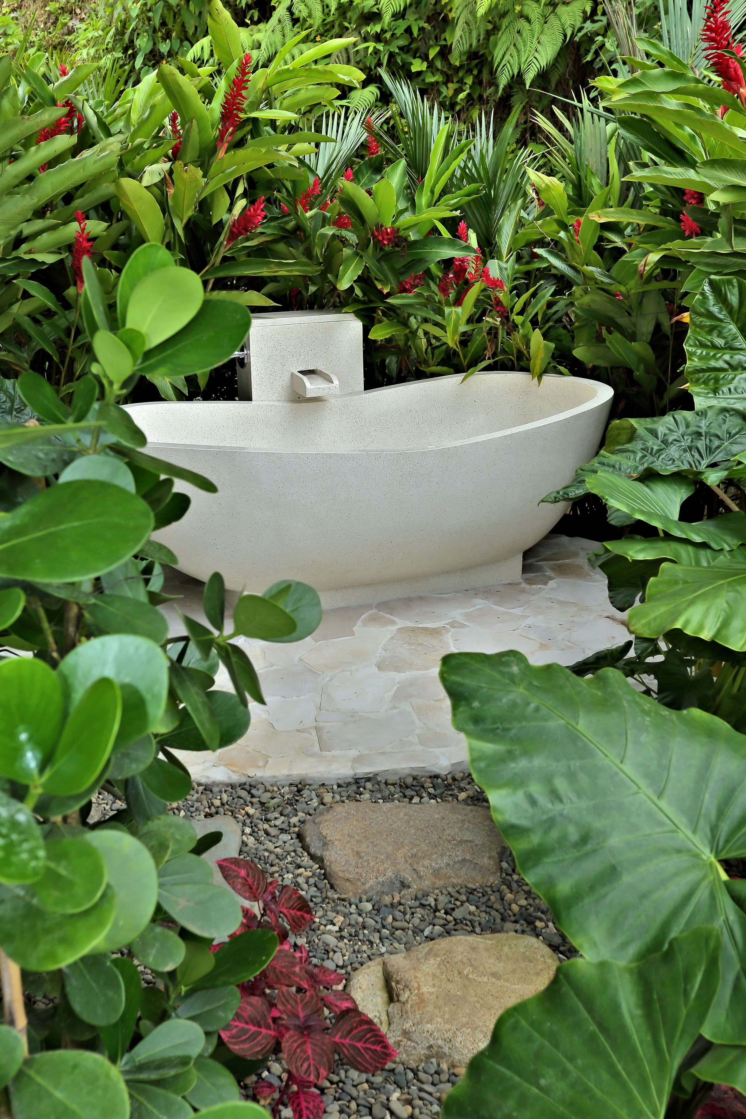 Un jardin agrémenté d’un grand pot blanc, entouré de différentes plantes vertes et de fleurs rouges.