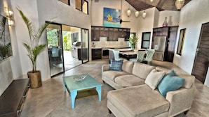 A spacious living area with a sofa, coffee table, and a large window overlooking a garden. - Golden Pineapple Villas (Bahía Ballena)