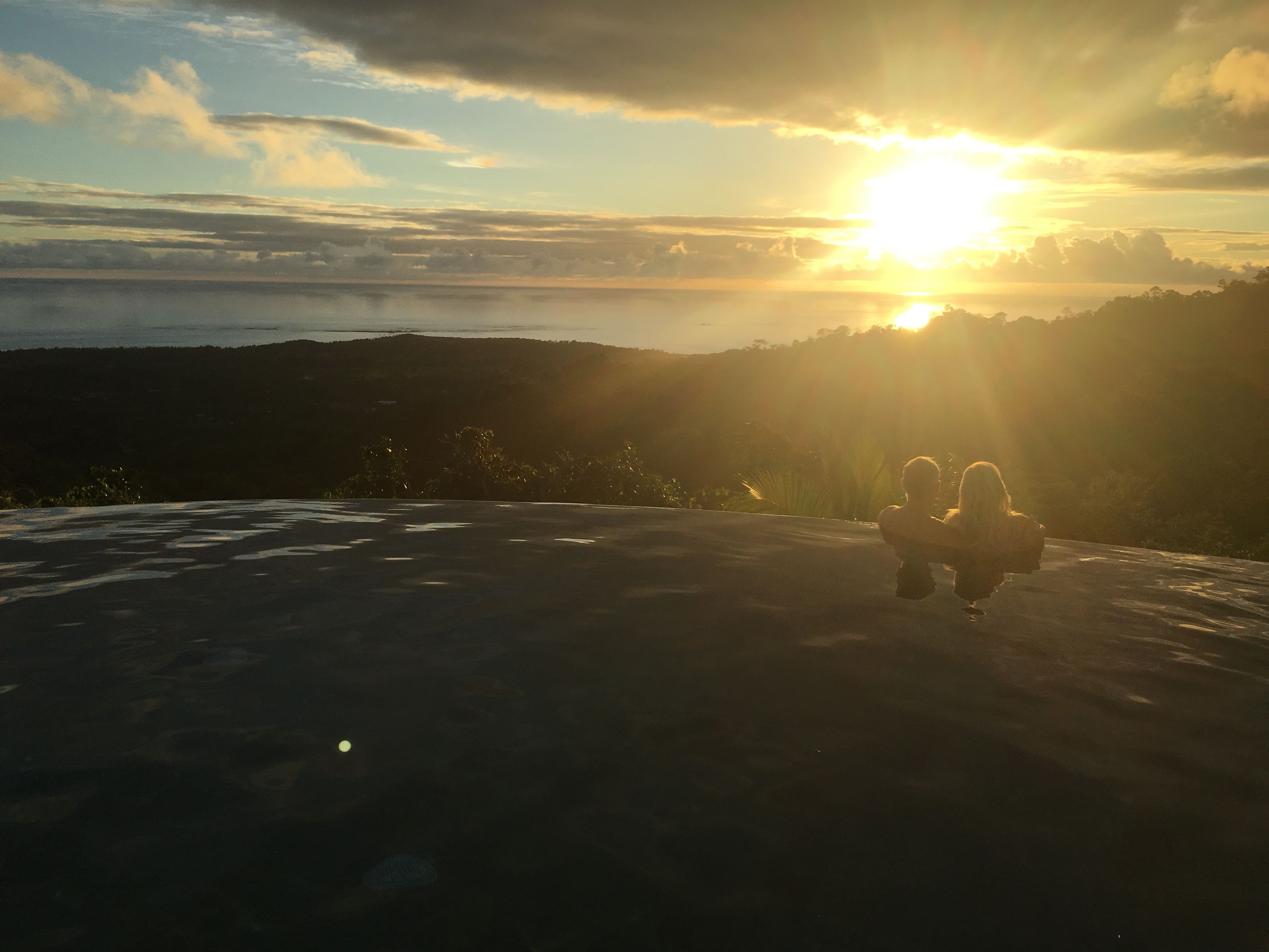 A sunset over a mountainous landscape with a person sitting on a flat surface.