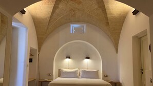 Un dormitorio con techo abovedado, una cama grande, mesitas de noche y un ventanal.