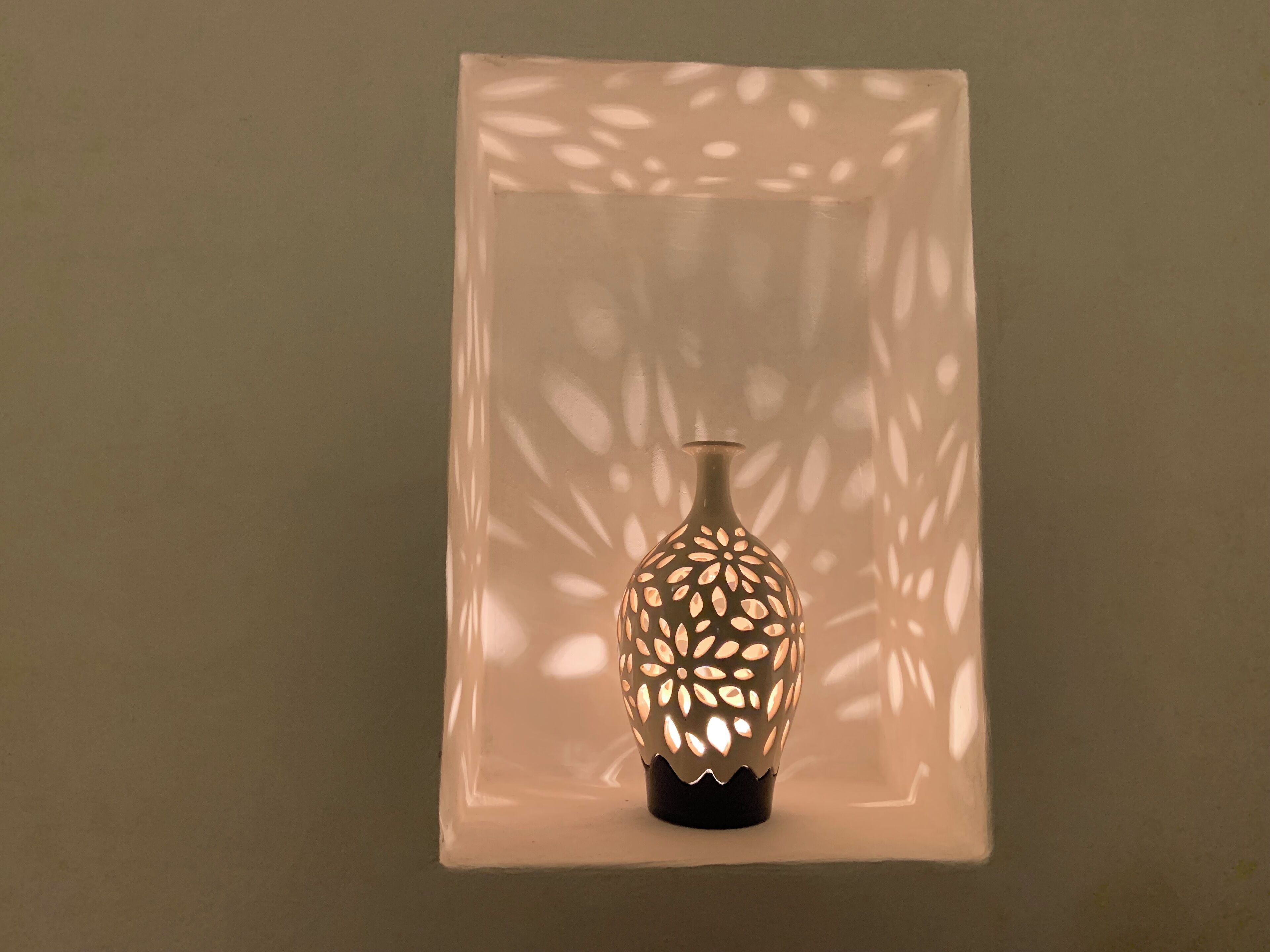 A decorative vase with a patterned cut-out design, placed on a flat surface against a plain background.