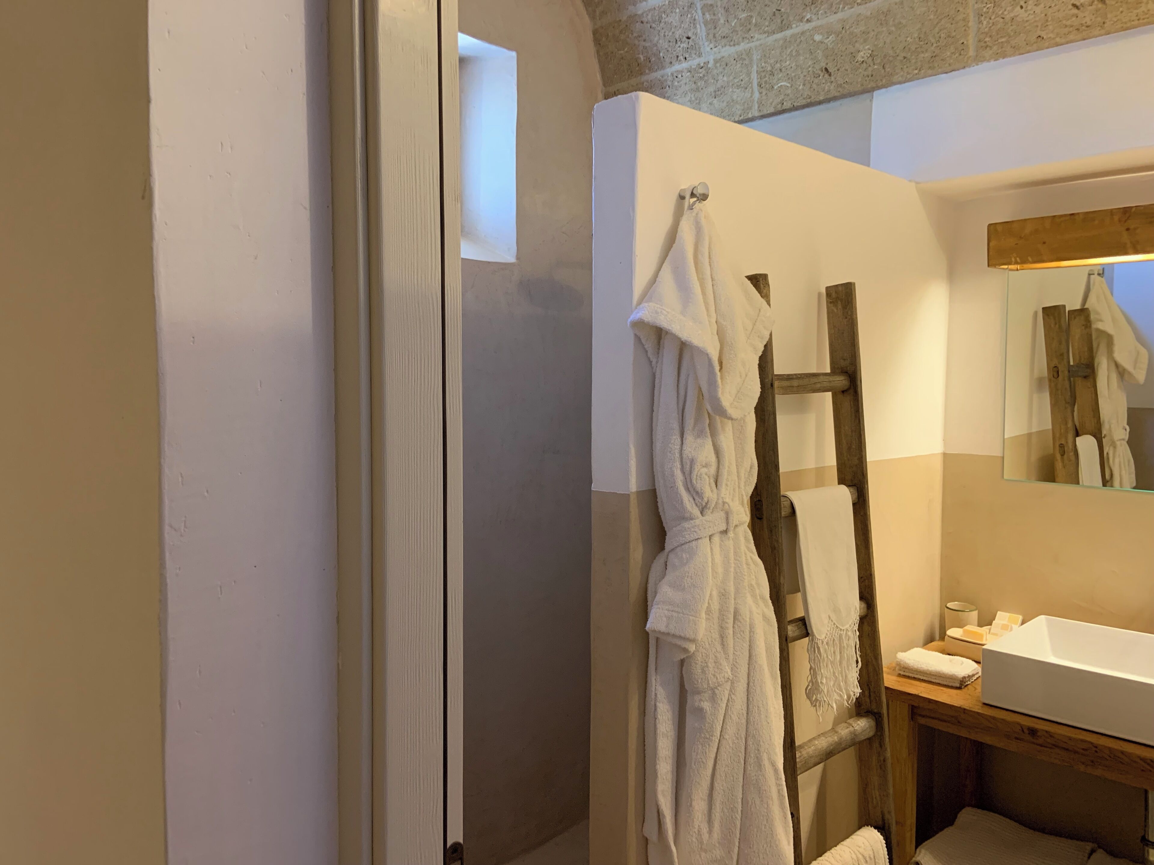Een badkamer met een houten ladder, een witte badkuip en een spiegel die een witte badjas weerkaatst.