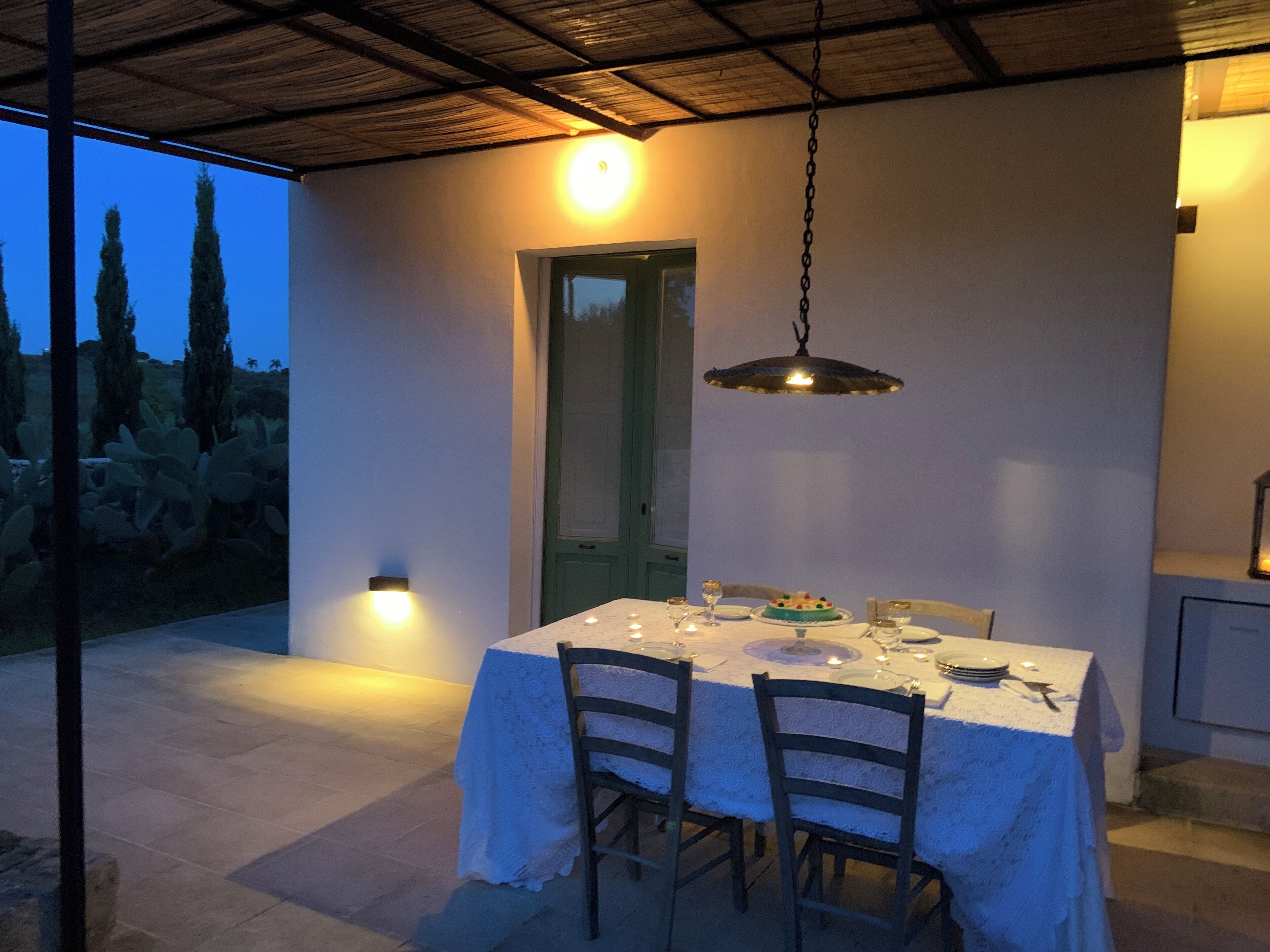 An outdoor dining area with a table set for two, a hanging light fixture, and a door leading to another room.