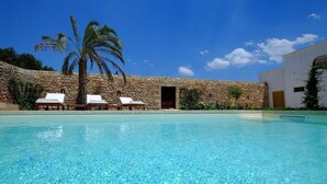 Piscina azul cristalina con sillas de descanso y un muro de piedra.
