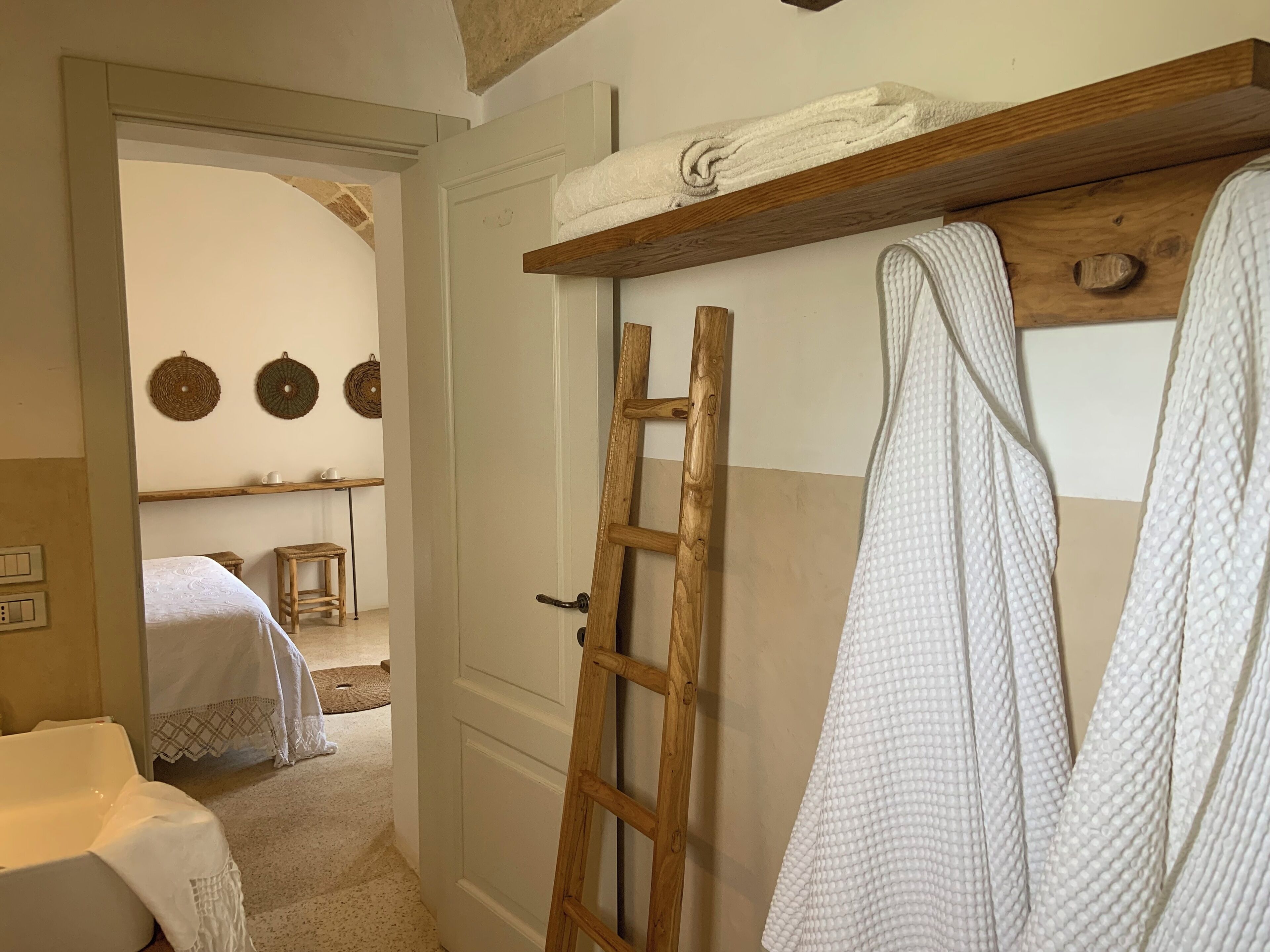 Un dormitorio con una escalera de madera, un baño blanco, una cama con cubierta blanca y un estante con toallas.