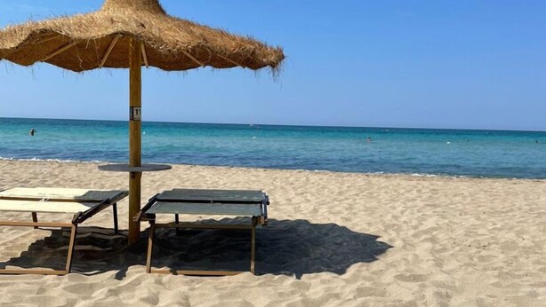 Una playa con una sombrilla de paja y dos sillones reclinables.
