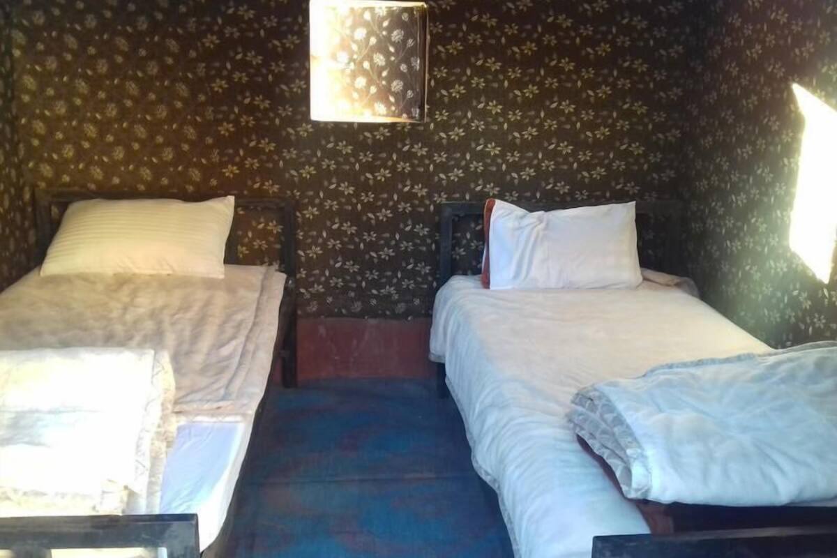 Une chambre avec deux lits simples, une petite fenêtre et un mur orné d’un motif floral.