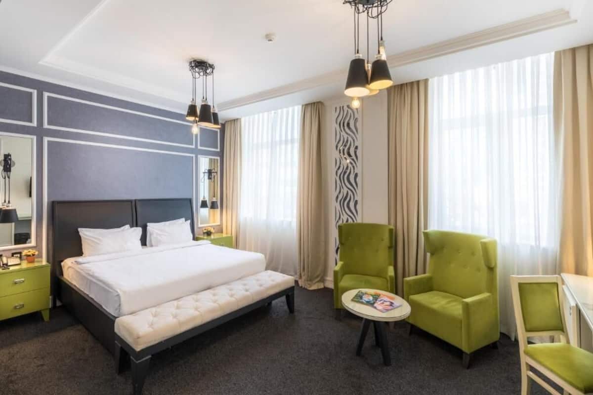 A hotel room with a large bed, two green armchairs, a small table, and a zebra-patterned wall.