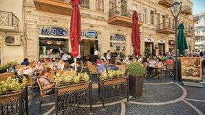 Un área de café al aire libre con varias mesas y sillas, rodeada de edificios con balcones.