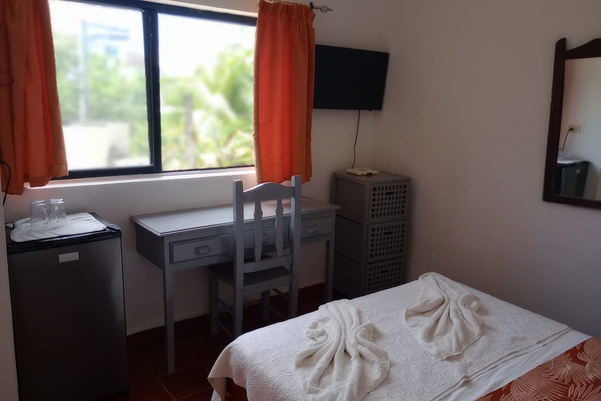 Een kamer met een bed, een bureau, een stoel, een televisie en een raam met gordijnen.