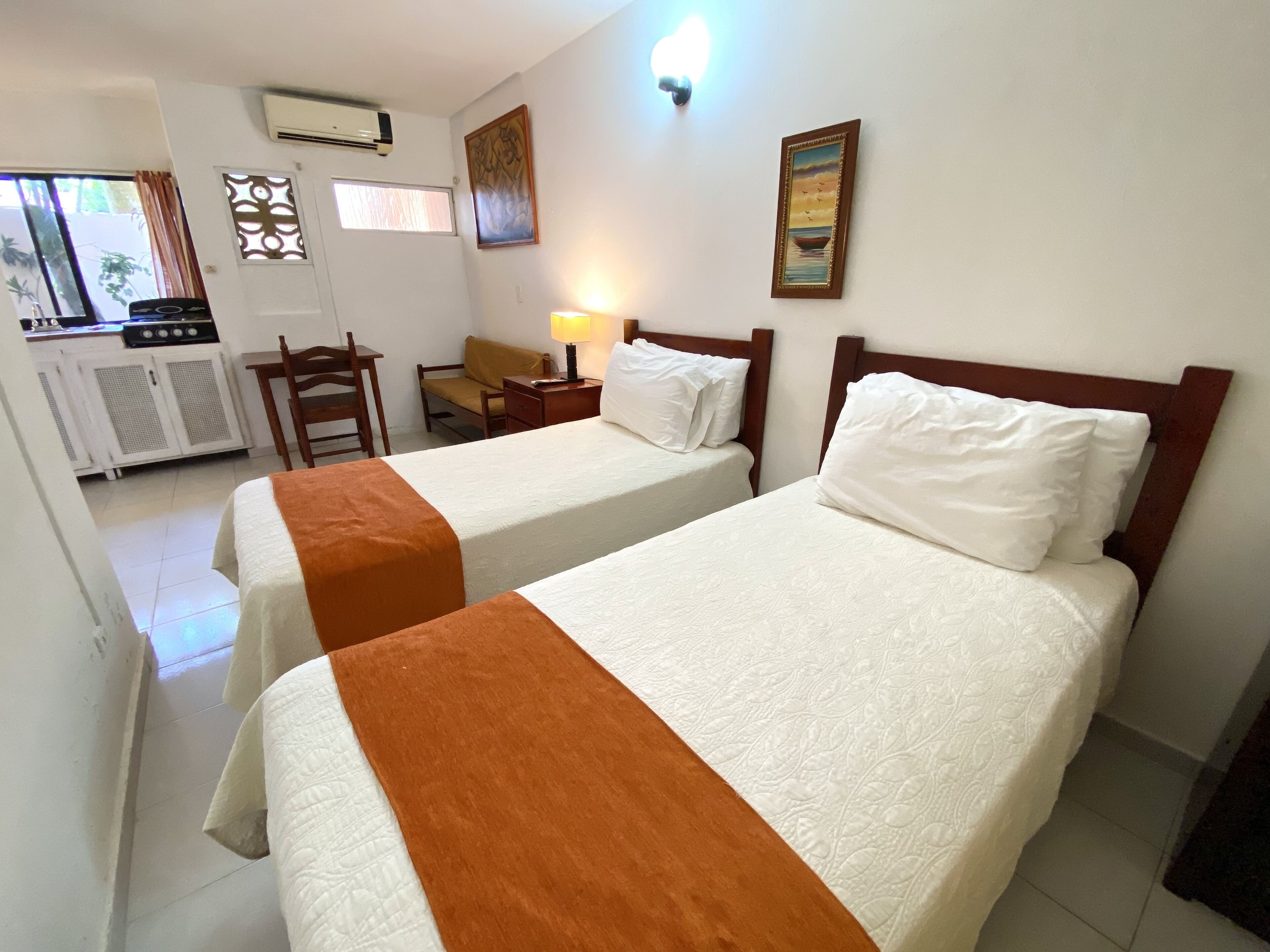 A hotel room with two beds, a desk, a chair, a lamp, and a window with curtains.