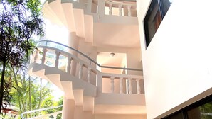A multi-level white building with a spiral staircase, a window with a curtain, and a fan on the ground floor. - Hotel Alegria (Cabarete)