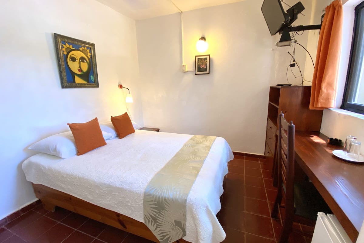 Een hotelkamer met een bed, een bureau, een televisie en een wandlamp.