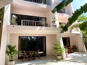 Un bâtiment à deux étages doté d’un balcon, de grandes fenêtres et d’un espace extérieur aménagé avec des chaises et des tables.