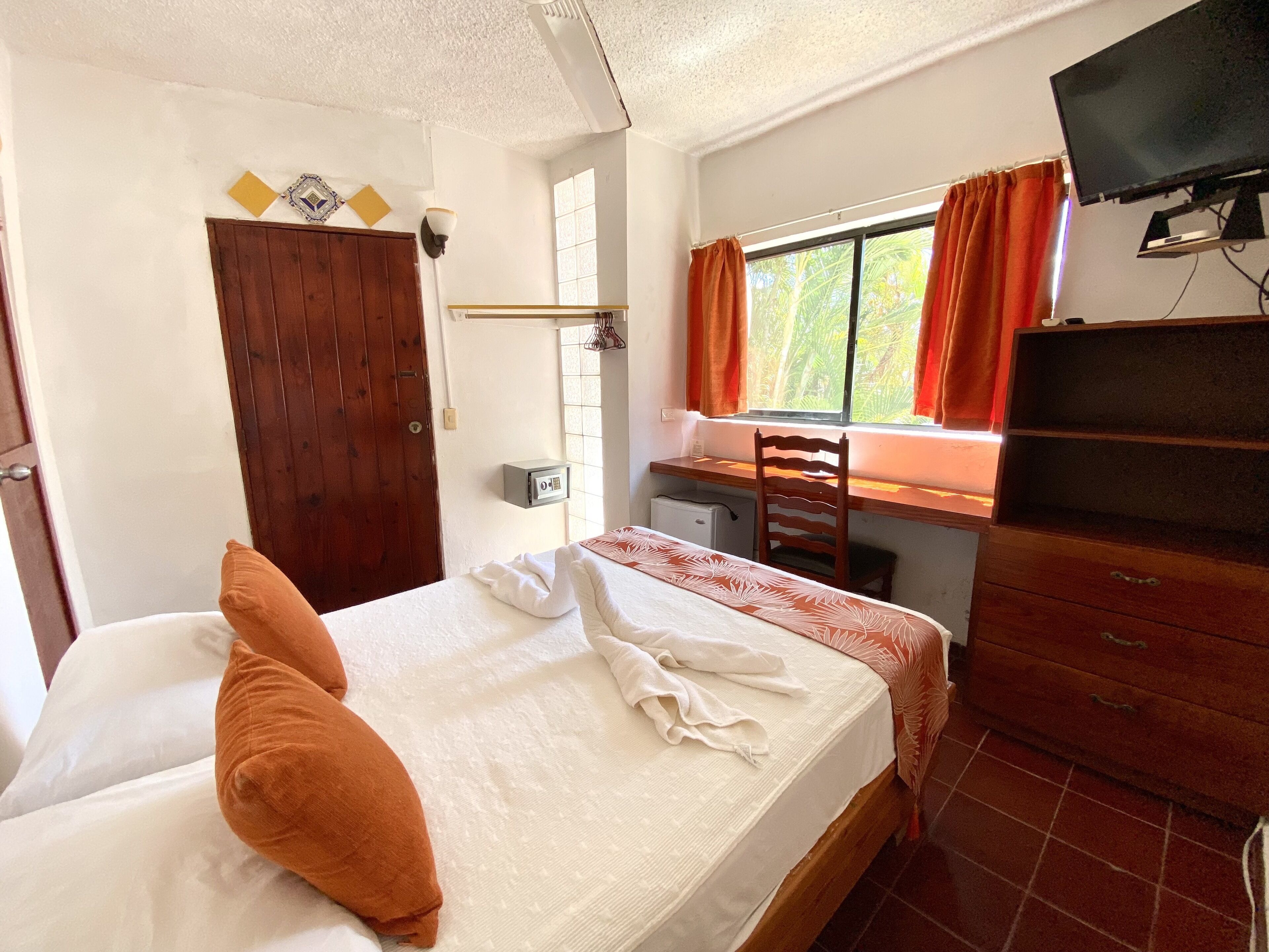 A hotel room with a bed, a desk, a chair, a television, and a window with curtains.