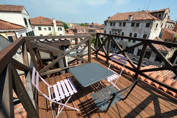 A wooden deck with a table and chairs, overlooking a cityscape with terracotta-roofed buildings. - ARNOLDI-Rooftop (Venice)