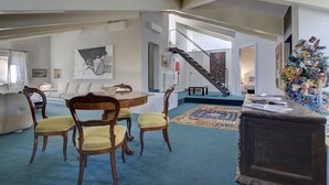 A spacious living area with a round table, wooden chairs, a sofa, and a staircase leading to another level. - ARNOLDI-Rooftop (Venice)