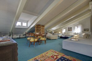A spacious attic room with a high ceiling, a dining table with chairs, a sofa, and a patterned rug.