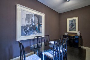 A dining area with a round glass table surrounded by chairs, framed artwork on the walls, and a dark floor. - ARNOLDI-Rooftop (Venice)