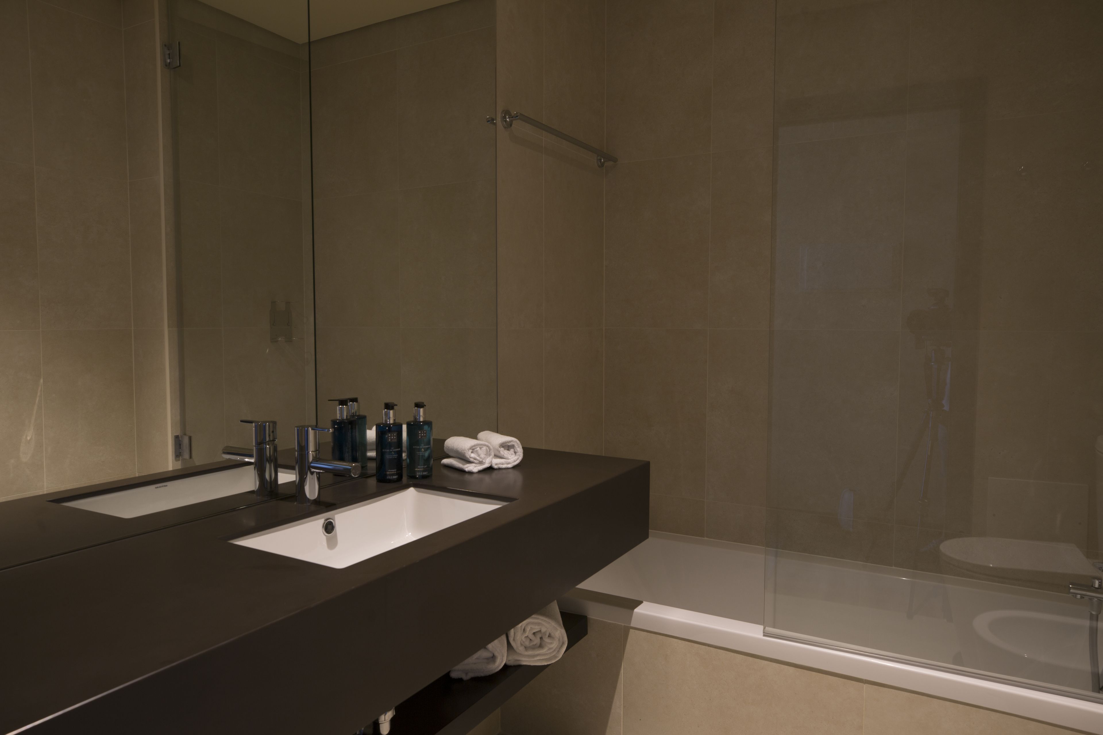 Un baño moderno con mostrador oscuro, dos lavamanos y ducha con mampara de vidrio.