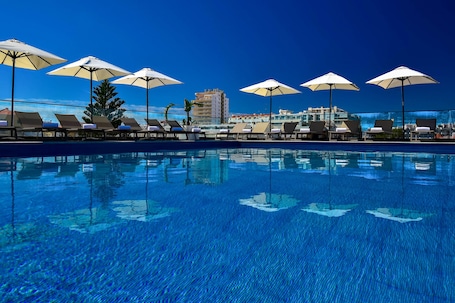 Una piscina techada, una piscina al aire libre, sombrillas