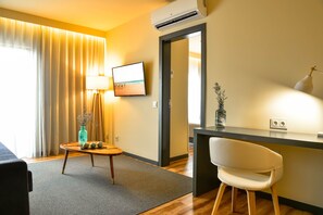 A hotel room with a desk, chair, lamp, TV, and a view of the outdoors.