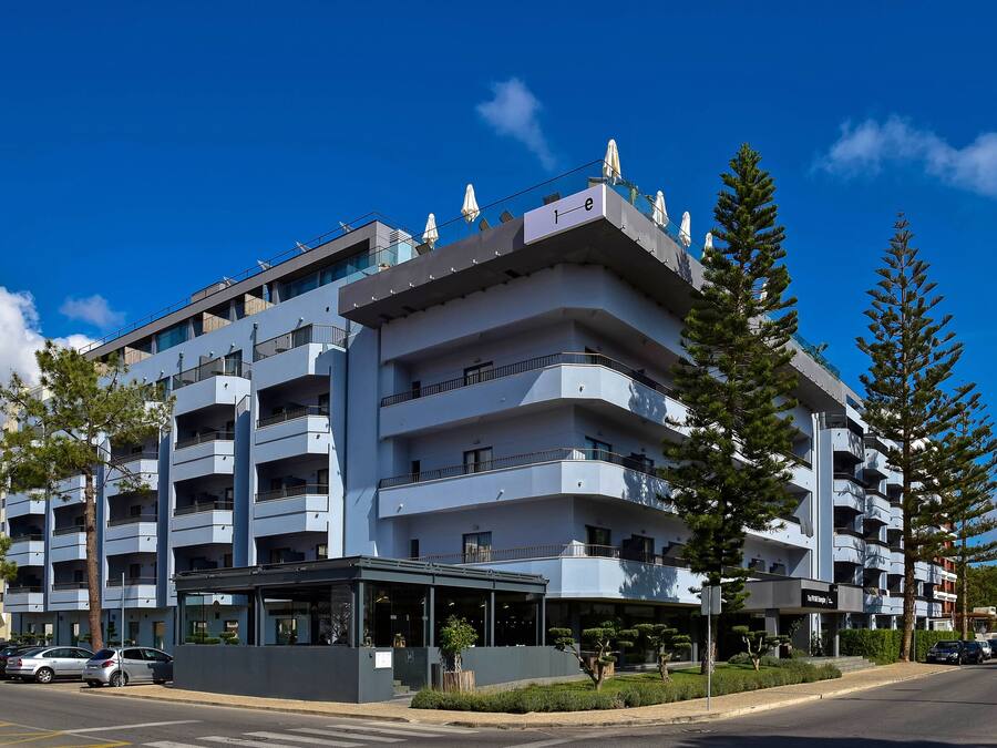 A multi-story hotel with balconies, a covered entrance, and a parking area.