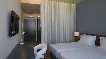 A hotel room with a bed, a desk with a chair, a TV, and a lamp.