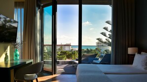 A hotel room with a bed, a desk, a chair, and a view of the sea and buildings. - The Prime Energize Hotel & Spa (Vila Real Santo Antonio)