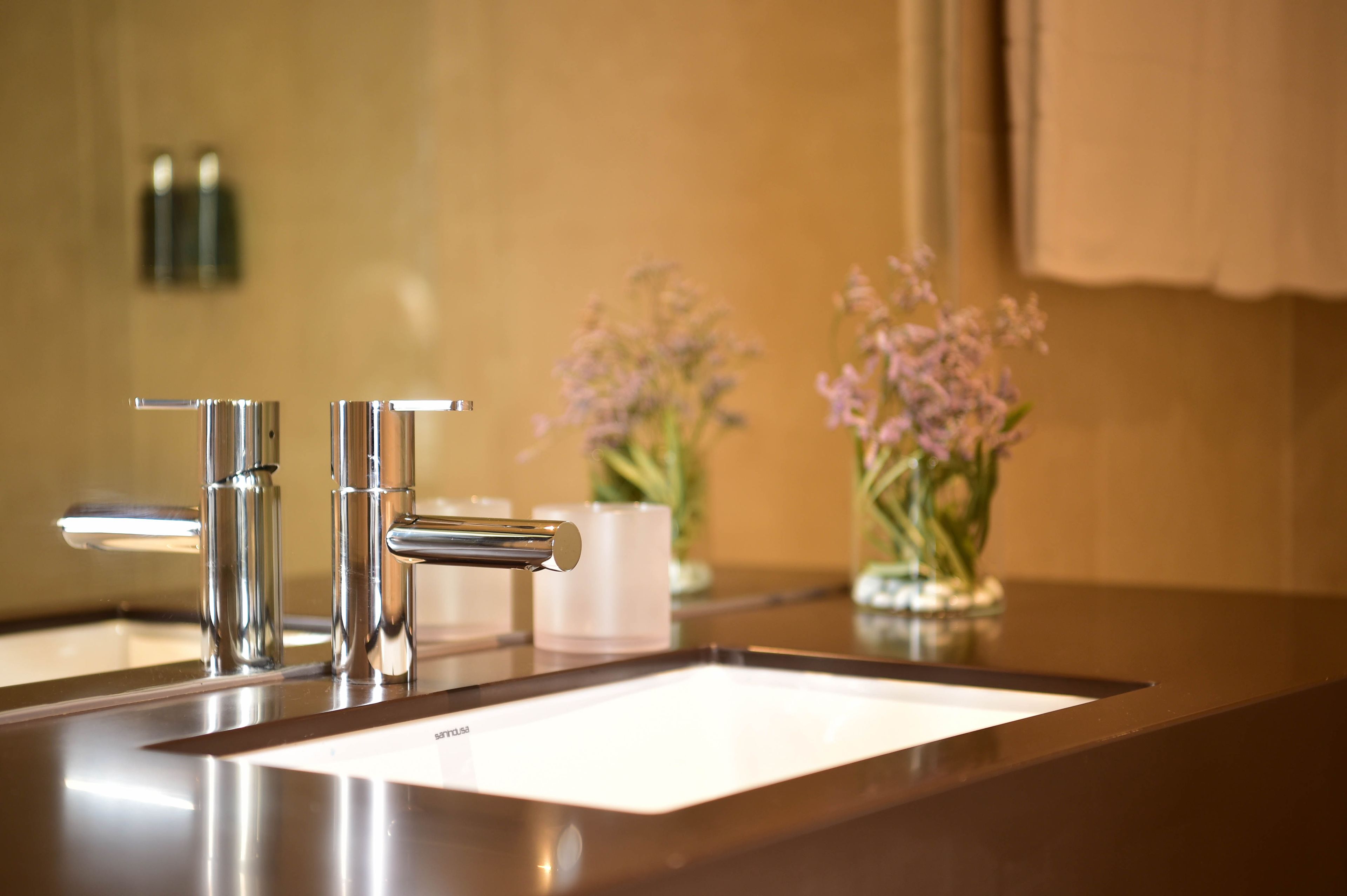 A modern bathroom with a stainless steel sink, two faucets, and a vase with flowers on the counter.