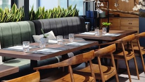A restaurant with a long wooden table, cushioned seating, hanging pendant lights, and a large window with a view. - The Prime Energize Hotel & Spa (Vila Real Santo Antonio)