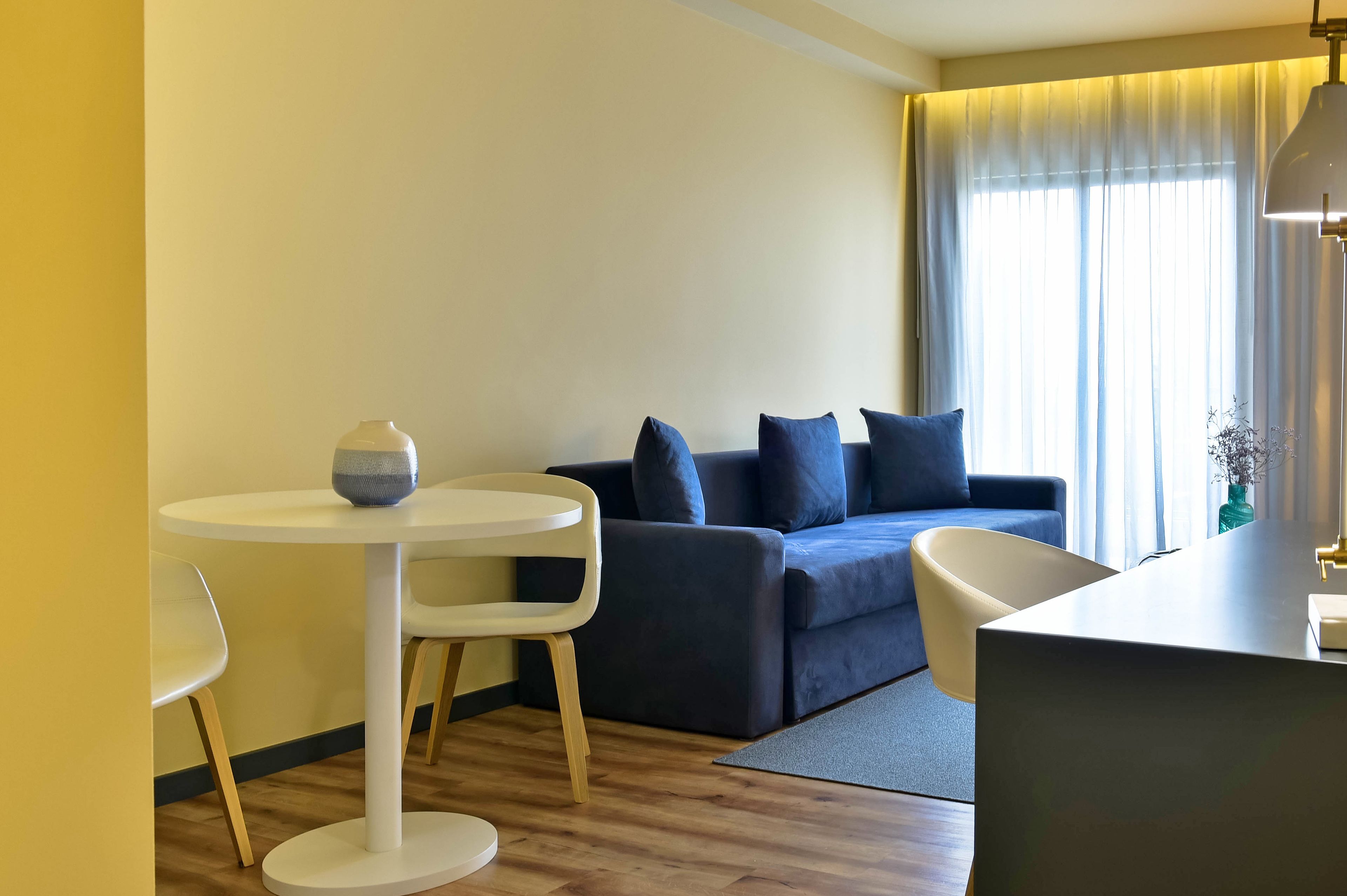 Een moderne woonkamer met een ronde witte tafel, een donkerblauwe bank met meerdere kussens en een witte fauteuil.