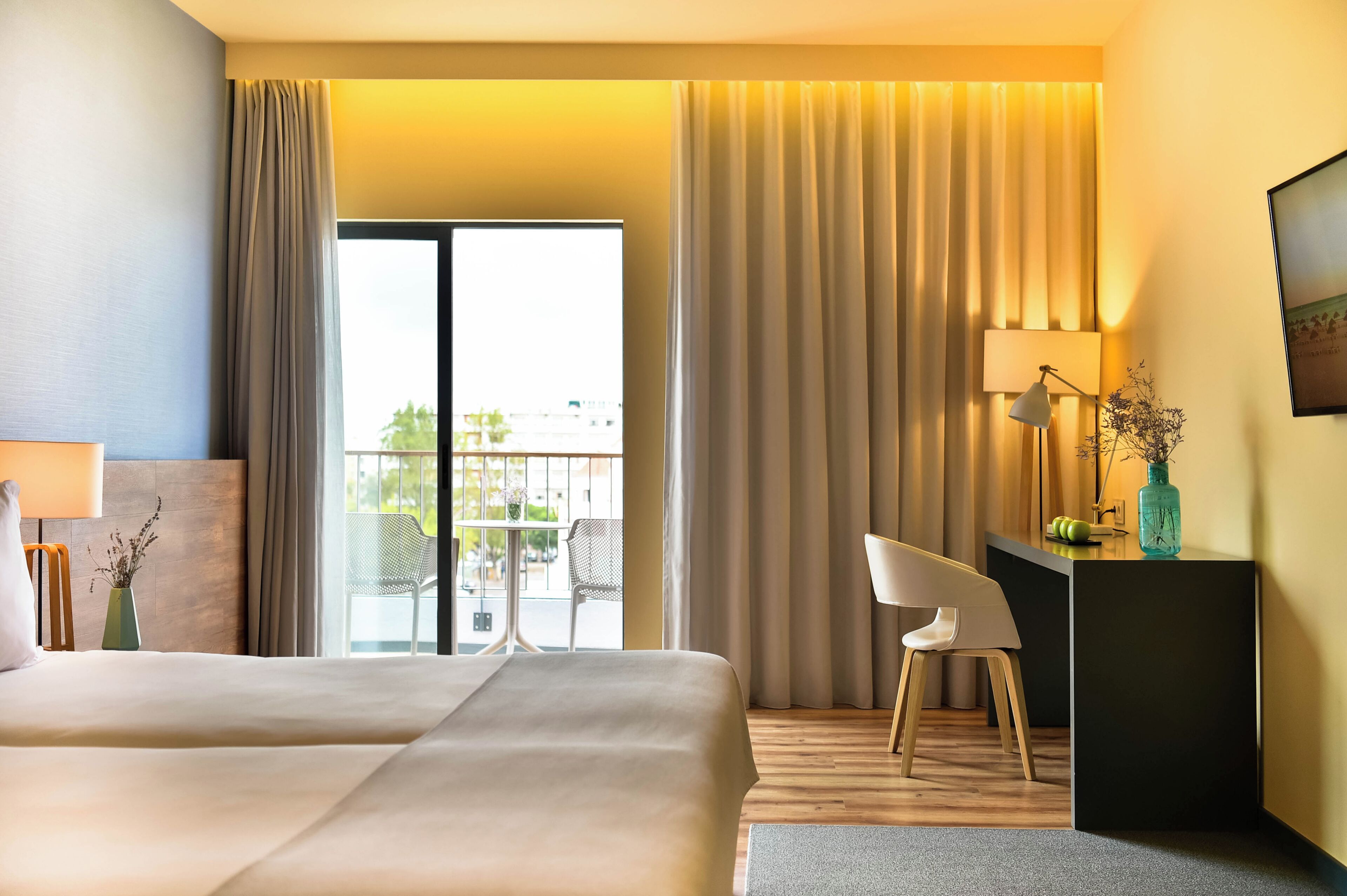 Ein Hotelzimmer mit zwei Betten, einem Schreibtisch, einem Stuhl, einer Lampe und Blick ins Freie.
