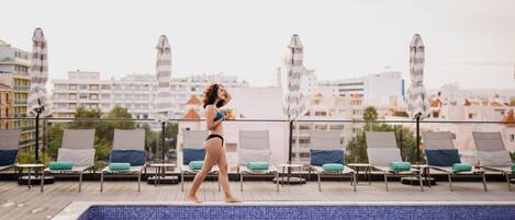 Zona de piscina al terrat amb gandules i ombrelles, amb vista a un paisatge urbà.