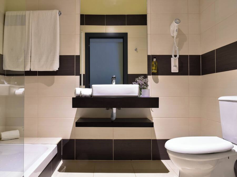 Un baño con bañera, lavamanos, inodoro y secador de pelo montado en la pared.