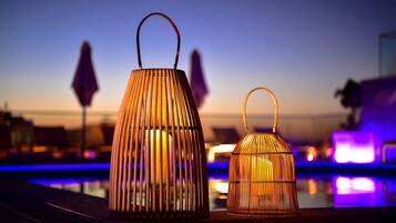 Dos faroles de mimbre con asas en un balcón con piscina y luces de la ciudad al fondo.