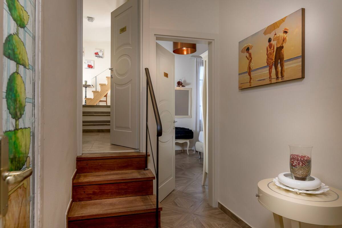 A hallway with wooden stairs, a white door, and a painting of two people on a beach.