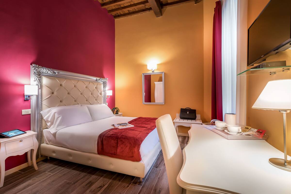 A hotel room with a bed, bedside table, desk, chair, and a TV.