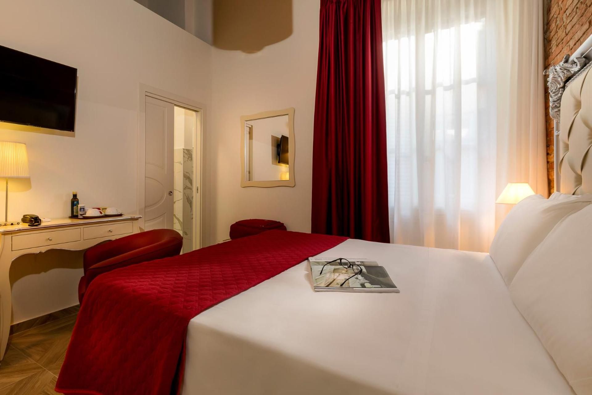 Une chambre d’hôtel avec un lit, un bureau, une chaise, une télévision et une fenêtre avec des rideaux.